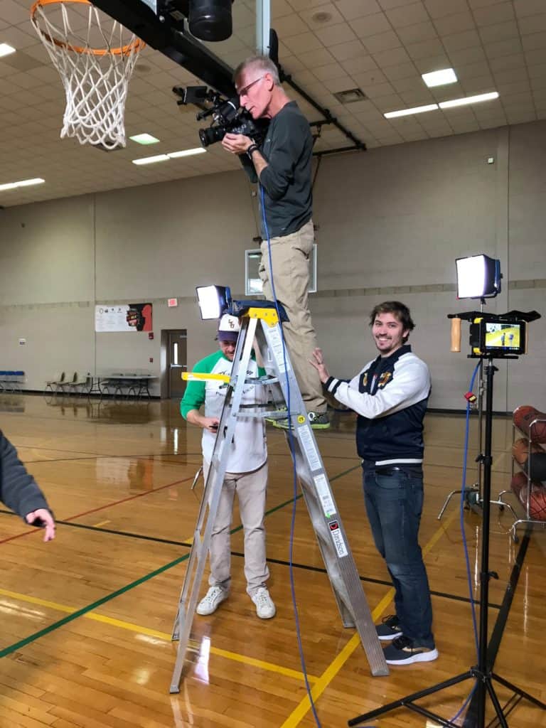 man on ladder in high school gym filming video